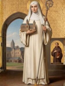 Święta Adelina z Mortain w jasnym habicie, z makietą kościoła i pastorałem.